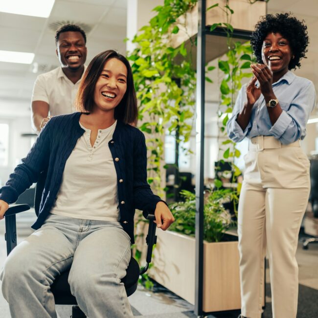 Asian woman enjoying office chair race at workspace and having fun
